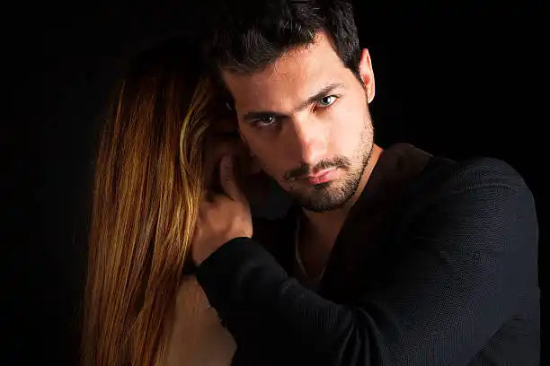 Un homme aux cheveux foncés et à la barbe, en chemise noire, avec son bras autour d'une femme.